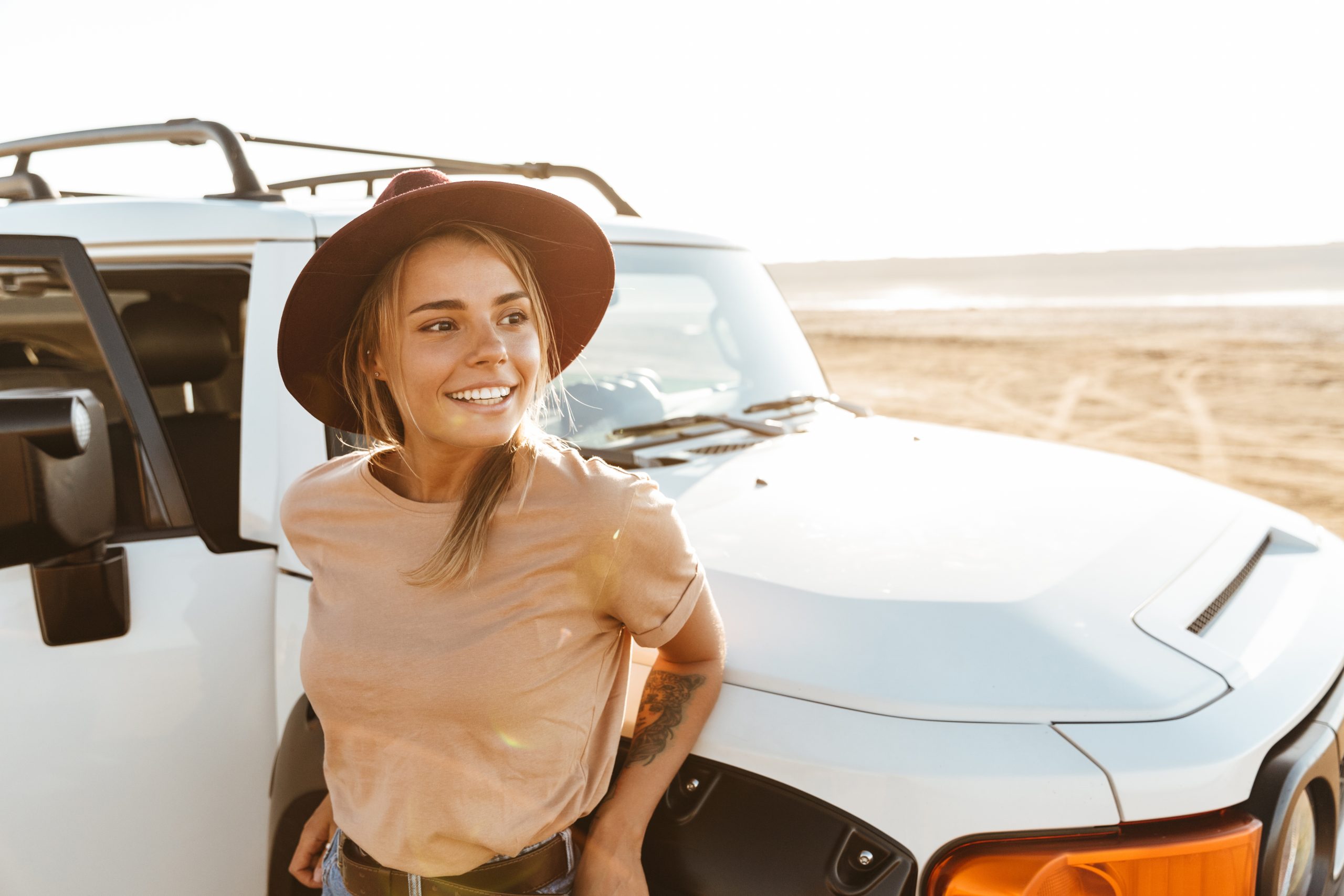 Beautiful young girl standing at the car at the sunny beach, holiday trip